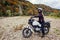 Woman biker travel by motorbike in fall. Motorcyclist enjoys autumn landscape in mountains having rest by forest