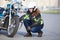 Woman biker trying to repair flat tire on motorcycle at city asphalt road