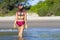 Woman and bikini crimson with hat walk on beach