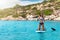 Woman in a bikini on a stand up paddle board over turquoise, Mediterranean waters