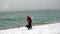 Woman in black and black dog walking on the beach during a snowstorm