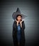 Woman with black cape and witch hat place two hands under her face on stripe metal background
