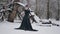 Woman in black dress in fairy tale image stands in snow in winter forest