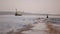 Woman in a black dress goes along the coastline on the background of water, the city and the industrial ship