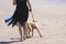 Woman in black dress leads dog on leash on the beach