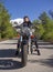 A woman in a black leather biker jacket on a chopper motorcycle in Greece on a road in the forest in the mountains