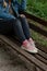 Woman in black ripped jeans and pink canvas sneakers sitting alone on  bench