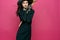 woman in black suit witch broomstick posing pink background