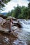 Woman in black and white striped dress and with straw hat on knee is sitting at stone near at Splashing Waterfall