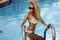 woman with blond hair in bikini and sunglasses posing in swimming pool