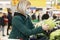 Woman blonde in a medical mask chooses vegetables in a supermarket. Healthy eating and vegetarianism. Quarantine during the