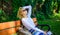 Woman blonde with sunglasses dream about vacation, take break relaxing in park. Girl sit bench relaxing in shadow, green