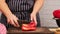 Woman in blue apron cuts ripe red bell pepper into pieces on wooden cutting board