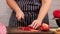 Woman in blue apron cuts ripe red bell pepper into pieces on wooden cutting board
