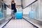 Woman with blue baggage suitcase on escalator