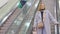 a woman in a blue coat descends the steps of an escalator in a shopping mall.