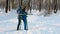 Woman in blue down jacket with hood is doing legs exercises on simulator in a winter Park Front view