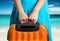 Woman in blue dress holds orange suitcase in hands on the beach