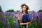 A woman in a blue dress on a purple field of lupins. Meadow with purple flowers in summer. A girl with long hair holds a bouquet