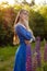 Woman in blue dress in purple lupines field. Meadow of violet flowers in the summer. Girl with long hair holding a lupine bouquet