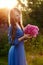 Woman in blue dress in purple lupines field. Meadow of violet flowers in the summer. Girl with long hair holding a lupine bouquet