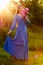 Woman in blue dress in purple lupines field. Meadow of violet flowers in the summer. Girl with long hair holding a lupine bouquet