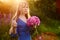 Woman in blue dress in purple lupines field. Meadow of violet flowers in the summer. Girl with long hair holding a lupine bouquet