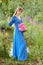 Woman in blue dress in purple lupines field. Meadow of violet flowers in the summer. Girl with long hair holding a lupine bouquet