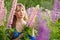 Woman in blue dress in purple lupines field. Meadow of violet flowers in the summer. Girl with long hair holding a lupine bouquet