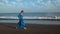 Woman in a blue dress runs along a black volcanic beach