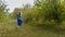 A woman in a blue dress runs through the rows of green trees.