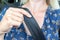 Woman in a blue dress sitting in car and wearing a seatbelt, safety belt in hand close up, automobile driver protection and safety