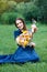 Woman in a blue dress is sitting in a meadow with flowers and drinking juice