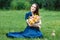 Woman in a blue dress is sitting in a meadow with flowers and drinking juice