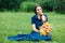 Woman in a blue dress is sitting in a meadow with flowers and drinking juice