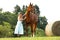Woman in blue dress stay beside her horse near hayroll