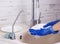 A woman in blue gloves washes a white plate under a stream of water over the sink