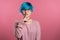 Woman with blue hair holding finger on her lips over pink background. Gesture of shhh, secret, silence. Close up.