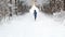 Woman in a blue jacket with hood runs along the path in park along the snowy alley in winter.