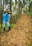 A woman in a blue jacket and jeans in a summer forest tries to photograph ants in a large anthill. On her head she has a mosquito