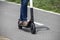 Woman with blue jeans and turquoise painted toenails rides an electric scooter down paved trail with grass at edge - cropped to