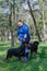 A woman in a blue sports uniform and two black dogs standing on green grass. Handler and adult female Rottweiler