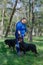 A woman in a blue sports uniform and two black dogs standing on green grass. Handler and adult female Rottweiler