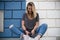 Woman with blue and white wall at the background sitting on a wall using her phone and surfing on the network - social network