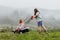 A woman in boots with her child in the form of a game mows the grass with a lawnmower in the garden