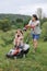 A woman in boots with her child in the form of a game mows the grass with a lawnmower in the garden