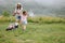 A woman in boots with her child in the form of a game mows the grass with a lawnmower in the garden