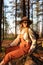 Woman botanist with backpack on ecological hiking trail in summer. Naturalist sitting on a tree trunk in forest