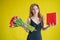 Woman with a bouquet of red tulips on a yellow background. Happy girl in a black dress holds an armful of flowers and a