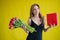 Woman with a bouquet of red tulips on a yellow background. Happy girl in a black dress holds an armful of flowers and a